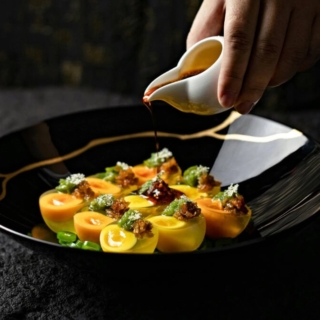 ein exquisit serviertes Hauptgericht auf einem dunklen, mit Sauce überzogenen Teller