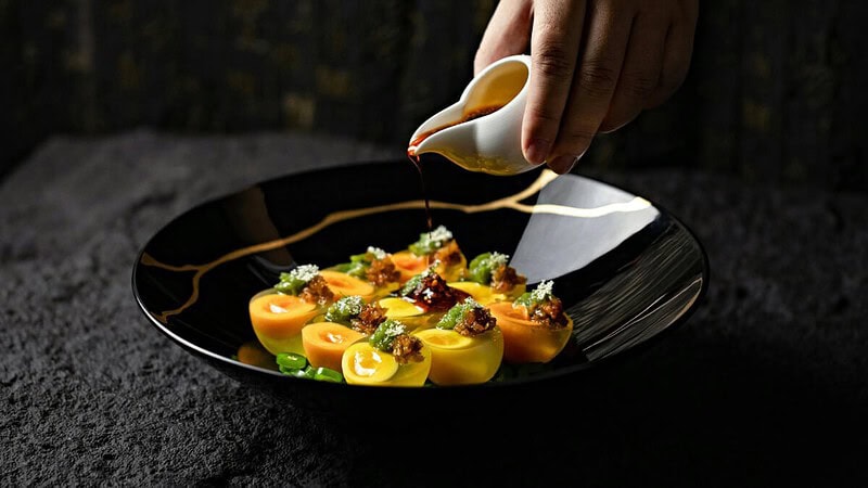 ein exquisit serviertes Hauptgericht auf einem dunklen, mit Sauce überzogenen Teller