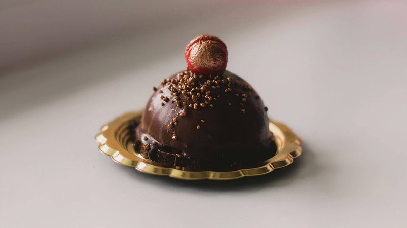 Schokoladenkugel-Dessert, serviert auf einem goldenen Teller, gekrönt mit einer karamellisierten Kirsche