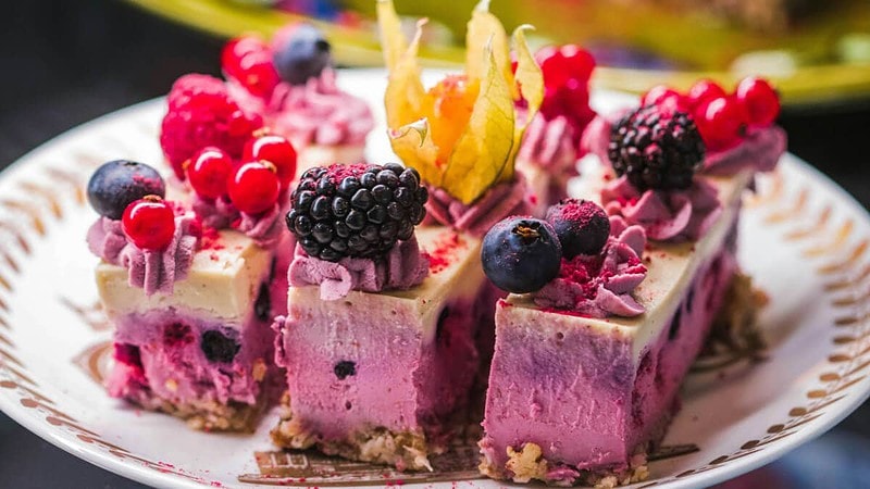Kuchen mit weißer Schokolade und Brombeeren, in Stücke geschnitten, mit Früchten und Physalis dekoriert