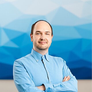 Mitarbeiter Paul Köhler schaut in die Kamera, bei blauem Hintergrund