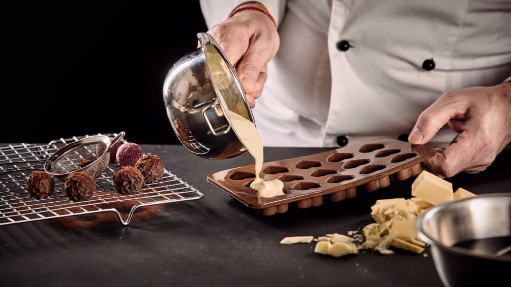 pralinen-seminar (2) Ein Konditor gießt Schokolade in eine Form, um Pralinen herzustellen
