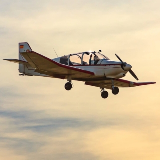 Ein Mann steuert bei Sonnenuntergang ein kleines Flugzeug und winkt in die Kamera