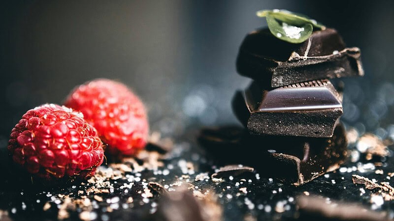 Zartbitterschokoladenstücke, daneben Himbeeren