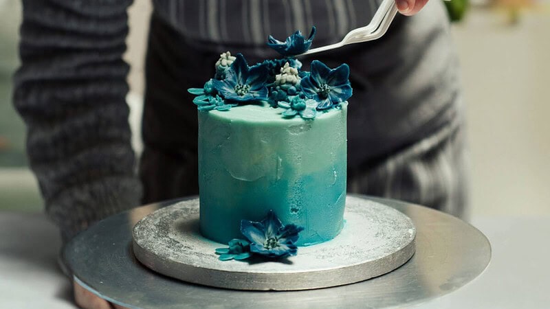 ein Mann dekoriert eine Torte mit essbaren Blumen aus Zuckerpaste