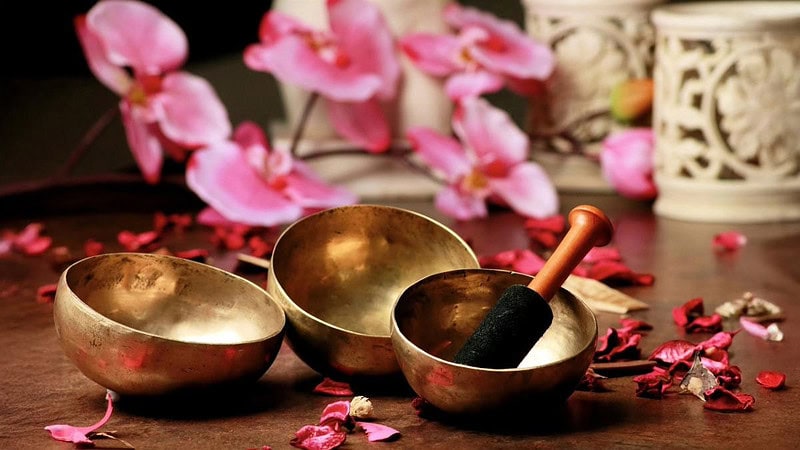 Drei unterschiedliche Klangschalen liegen auf einem Tisch der mit Blühten bedeckt ist.