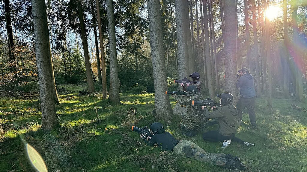 Lasertag-Teambuilding- Spieler zielen Fünf Lasertag Spieler mit Gewehren in der Hand die in Tarnkleidung gekleidet sind und alle in eine Richtung zielen. Sie befinden sich alle im Wald.