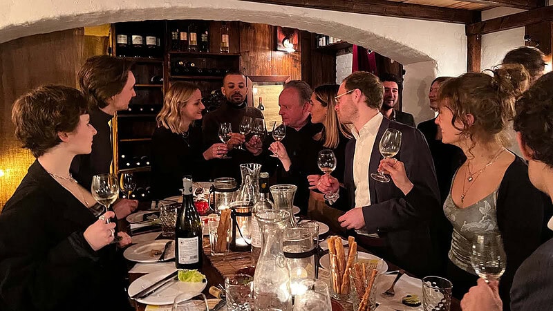 Eine Gruppe schick angezogener Leute, stößt in einem gemütlichen Wein Lokal an.