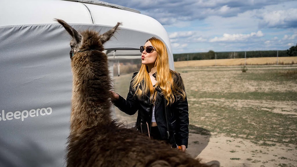 uebernachtung--Frau mit Alpaka Eine Frau streichelt ein Alpaka vor dem Sleep Cube.