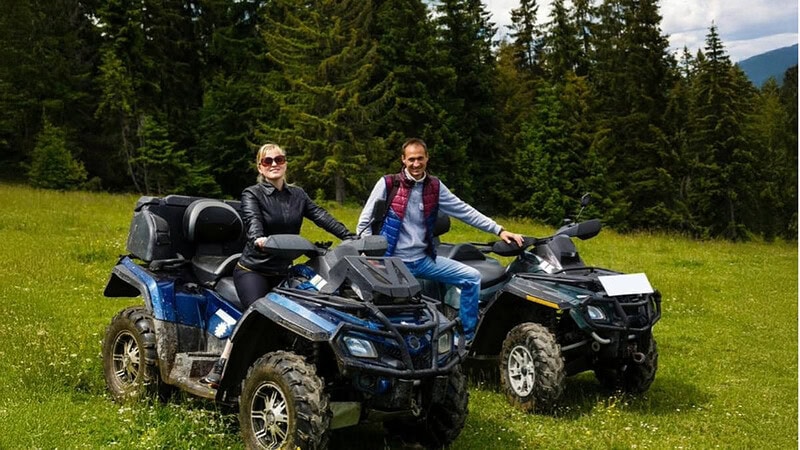 Ein Paar das mit ihren Quads auf einer Wiese steht und in die Kamera lacht.