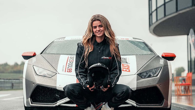 Eine Frau kniet in Rennkleidung und Helm vor einem Lamborghini Huracan.