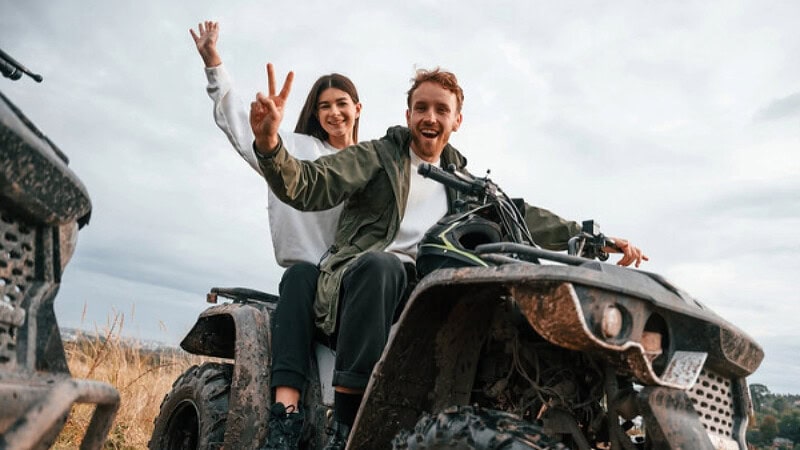 Ein Mann und eine Frau auf einen Quad die lachen und Peace mit ihren Händen zeigen.