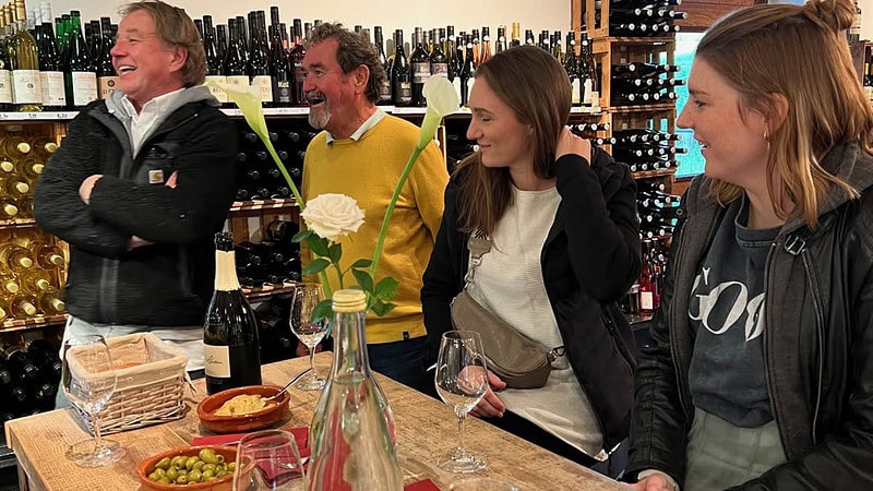 Gruppe die lachend an einem Tisch mit Wein und Snacks steht