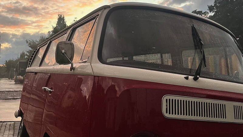 Nasser VW Bulli unter orangenem Himmel