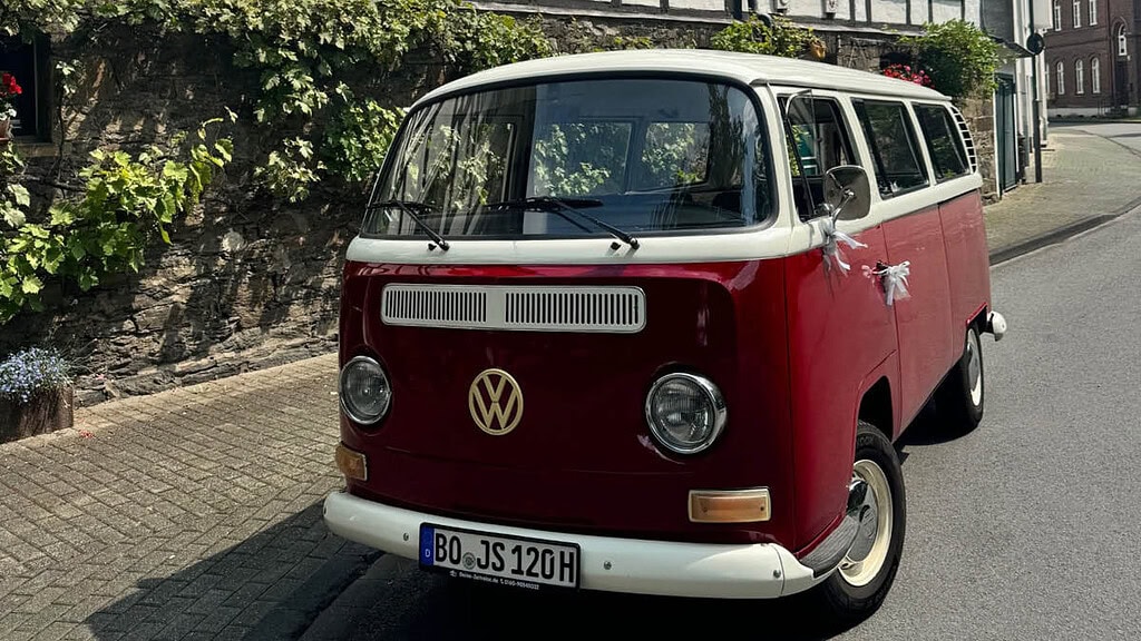 Deine Zeitreise- Bulli vor Haus Roter mit Schleifen verzierter VW Bulli Parkt am Straßenrand.
