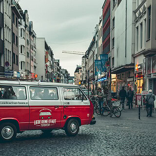 VW Bulli der über einen Stadtplatz fährt.
