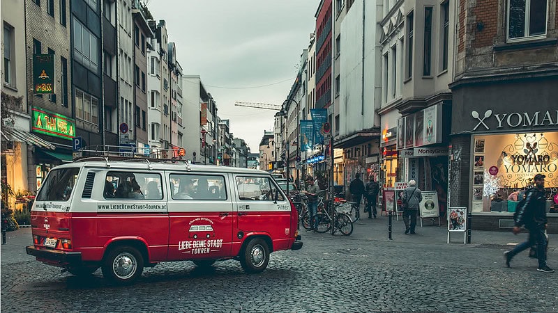 VW Bulli der über einen Stadtplatz fährt.