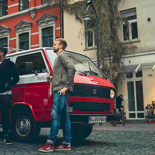 Eine Gruppe die neben einem VW Bulli steht und sich ein Gebäude anschaut.