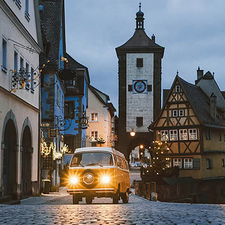 VW Bulli der durch eine Weihnachtlich geschmückte Straße fährt.