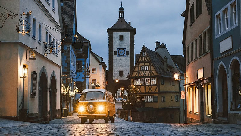 VW Bulli der durch eine Weihnachtlich geschmückte Straße fährt.
