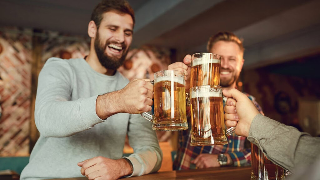maenner-geniessen-bier 3 Männer feiern zusammen in einer Bar und stoßen mit Bier an