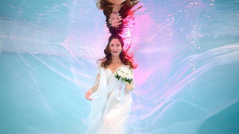 Frau im Hochzeitskleid mit Blumenstrauß unter Wasser Foto