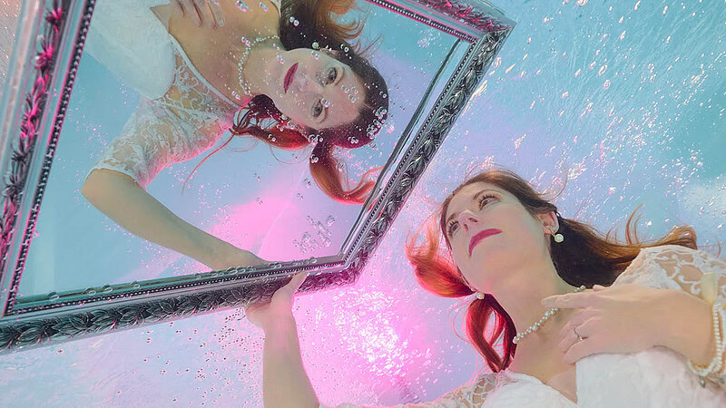 Frau im Hochzeitskleid die in einen Spiegel schaut Unterwasserfoto