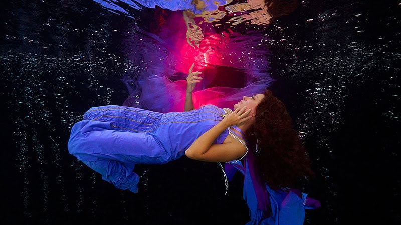 Eine Frau posiert im Dunkeln beim Unterwasser Fotoshooting.