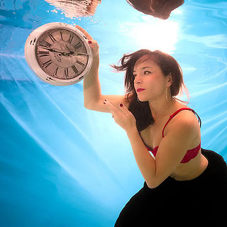Eine Frau posiert mit einer runden Uhr beim Unterwasser Fotoshooting.
