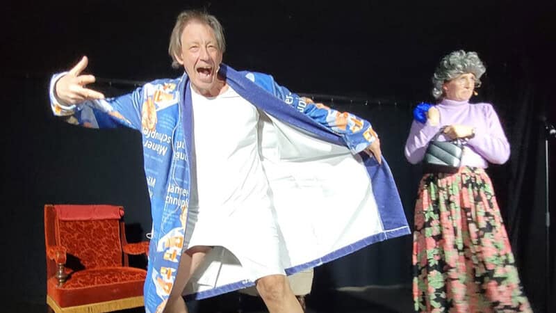 Auf der Bühne ist de rMann und eine Frau, der Mann öffnet seine Jacke