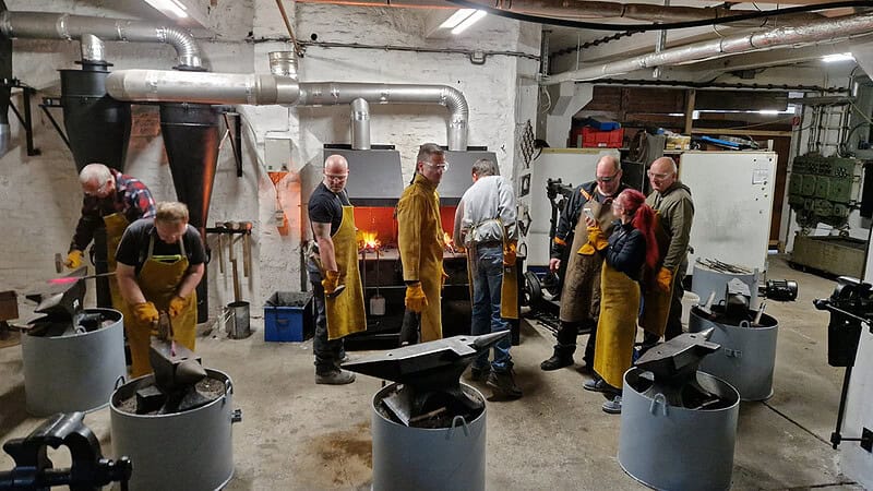 Eine Gruppe von Personen, die gerade beim Schmiedekurs bei Dresden ist. Alle sind am Arbeiten oder zeigen sich gegenseitig Ihre Werkstücke