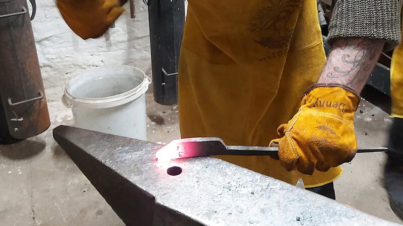 Ein Mann schläft mit dem Schmiedehammer auf das Werkstück zur Herstellung und Formung des Messers