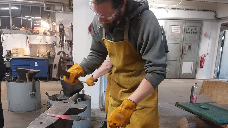 Ein Mann mit Schutzbrille und -Schürze schläft auf das Werkstück, um es in Form zu bringen