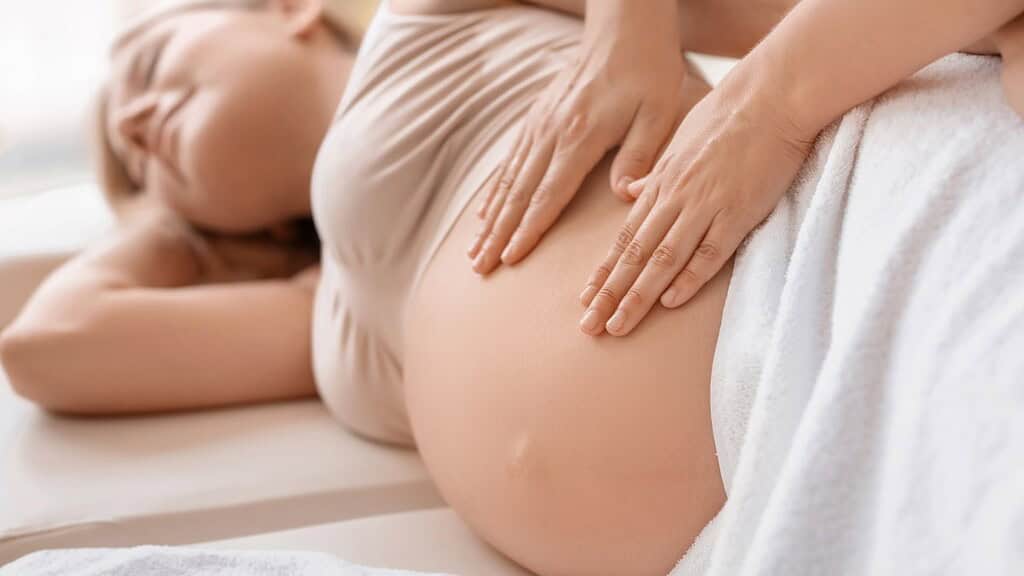 Schwangerschaftsmassage-2 Frau, die Schwanger ist und auf der Seite liegt wird sanft massiert