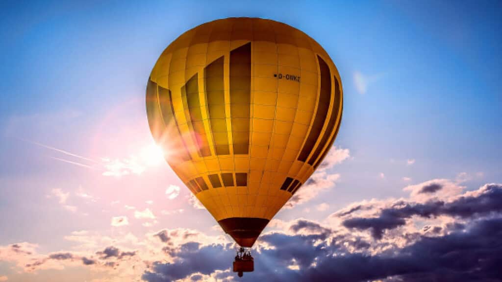 Gelber Ballon im blauen bewölkten Himmel mit Sonnenstrahlen.