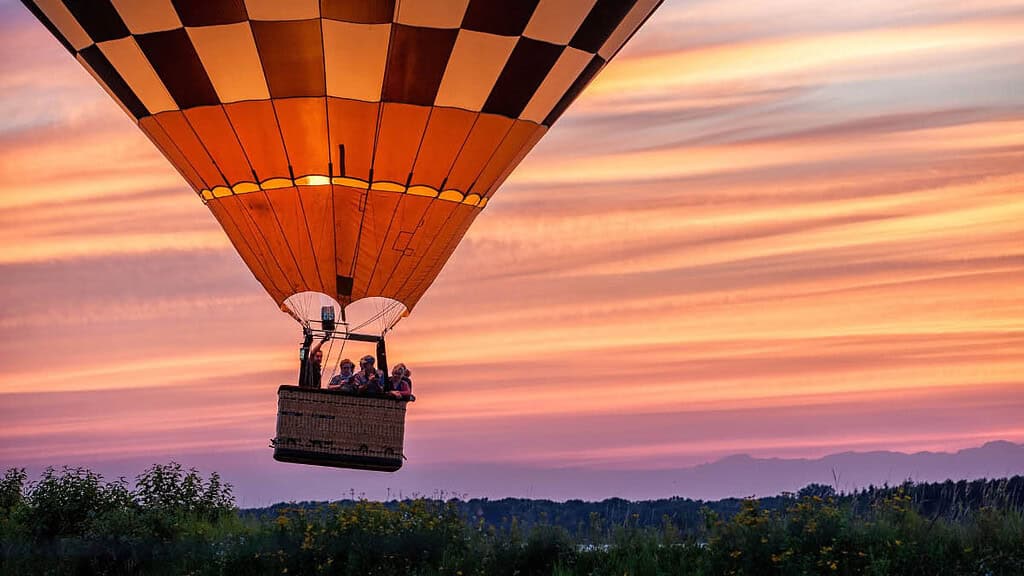 Ballonfahrt- Menschen im Ballon Menschen in einem bunten Ballon über einem Waldabschnitt bei Sonnenuntergang- Ballonfahrt- Menschen im Ballon
