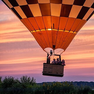 Menschen in einem bunten Ballon über einem Waldabschnitt bei Sonnenuntergang- Ballonfahrt- Menschen im Ballon
