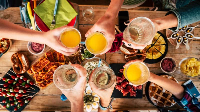 Gläser die über einem mit Essen und Snacks gedecktem Tisch anstoßen