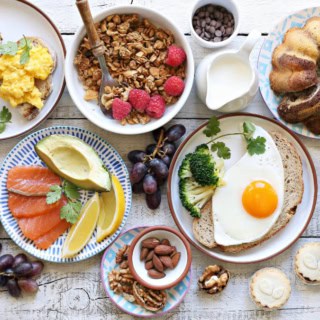 Gedeckter Tisch von oben mit Brot, Kuchen, Obst, Gemüse, Wurst, Käse und Müsli