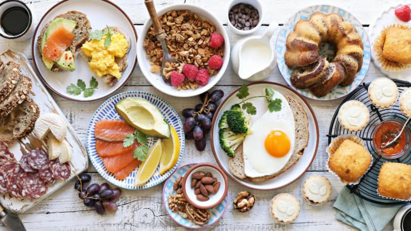 Gedeckter Tisch von oben mit Brot, Kuchen, Obst, Gemüse, Wurst, Käse und Müsli