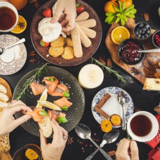 Gedeckter Tisch mit Kulinarischen Köstlichkeiten und Händen die sich Essen nehmen.