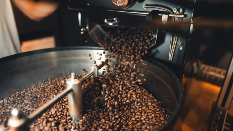 Frisch geröstete Kaffeebohnen fallen aus einer Röstmaschine in einen Auffangbehälter.