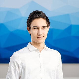 Mitarbeiter Leonard Gerlach schaut in die Kamera und ist glücklich. Blauer Hintergrund, weißes Hemd