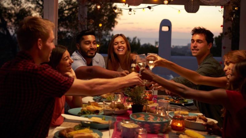 Freundesgruppe die an einem Gedecktem Tisch anstößt.