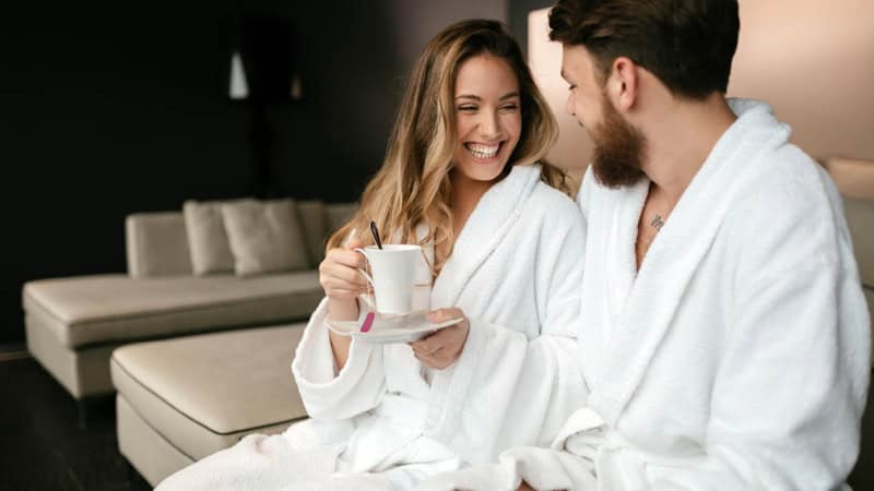 Ein Paar welches im Bademantel Tee trinkt und lacht.